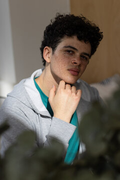 African American male sitting on sofa in living room with plant leaves wearing hoodie and t-shirt