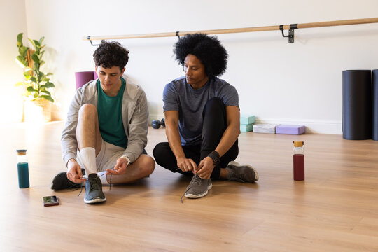 African American men sitting on light wood floor tying athletic shoes in barre studio with bottles