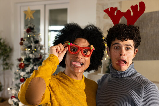 African American male friends posing, holding red glasses while wearing antlers at home