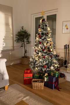 Snow-frosted Christmas tree is glowing in living room with gold star topper and wrapped gifts
