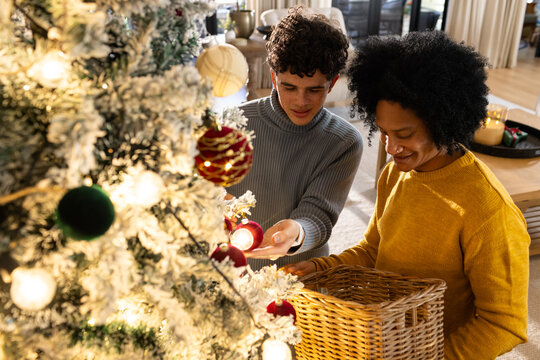 African American men in sweaters decorating tree at home holding wicker basket with ornaments