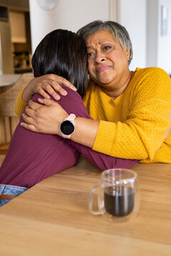 Senior African American woman embracing family at kitchen table in yellow sweater holding glass mug