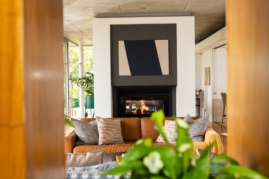 Tan leather sofa is sitting centered in living room framed by wooden jambs with fireplace, pillows
