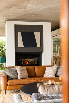 Brown leather sofa is sitting before black-framed fireplace, with textured pillows and coffee table