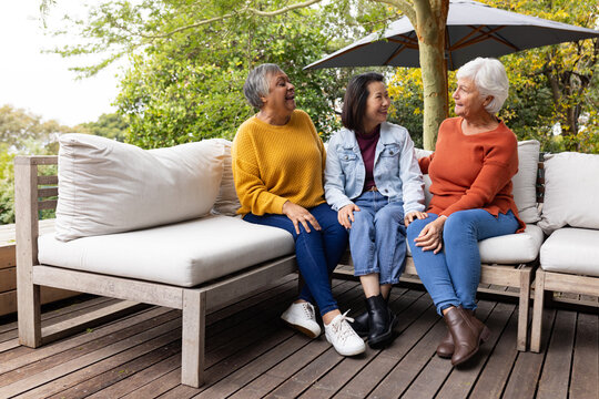 Diverse female friends, two mature women and one senior, chatting on wooden deck with modular sofa