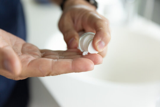 Senior Asian man squeezing cream from tube into palm at sink wearing dark sleeve and wristwatch