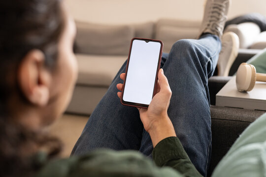 Smartphone showing blank white screen resting on sofa in living room beside headphones and notebook