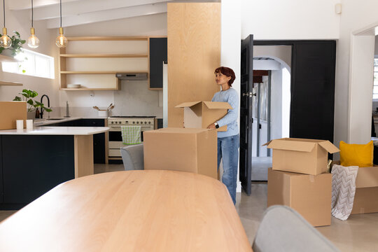 African American woman wearing light blue sweater carrying open moving box in kitchen, copy space