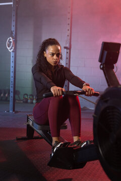 African American woman rowing on ergometer in gym, gripping handle and wearing fitness tracker