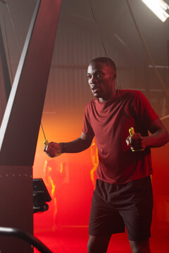 Adult African man wearing red shirt, black shorts holding yellow rope handles in fitness studio