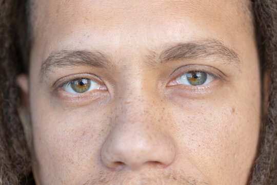 Man holding neutral expression in close-up showing dreadlocked hair and hazel-green eyes