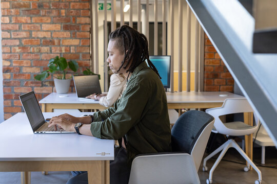 Diverse coworkers working in shared office, African man in olive-green shirt typing on laptop