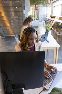 African coworkers typing on laptops with monitor, beige blazer, USB-C dock at co-working desk