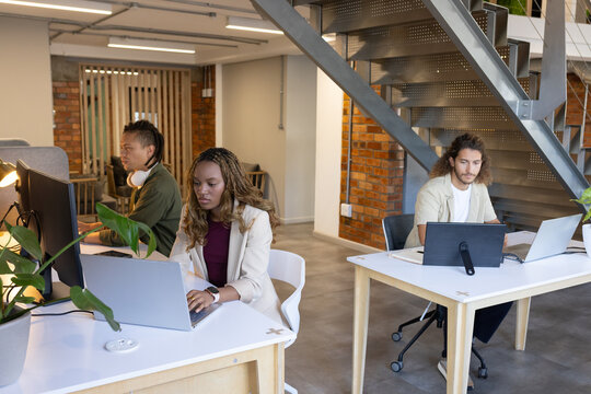 Diverse coworkers including woman in light blazer typing on laptop at open-plan office with monitor