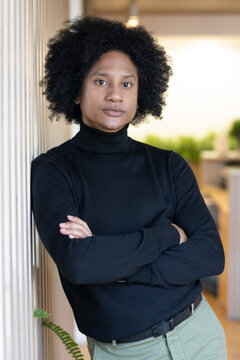 African American man standing against wood-slat wall in office, wearing black turtleneck