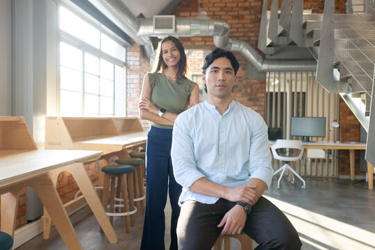 Team in open loft near windows and bench desks, sitting and standing wearing office attire smiling