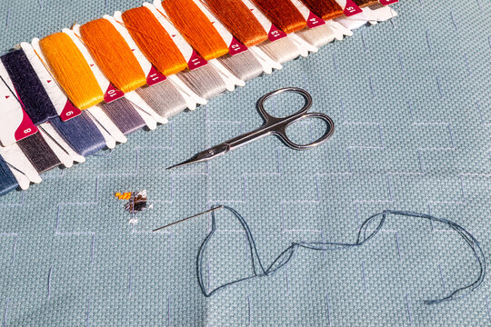 Close-up of embroidery threads, needle and scissors on aida cross stitch fabric with stitching