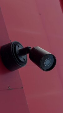 Wall mounted security camera on magenta exterior surface with angled bracket and dark lens