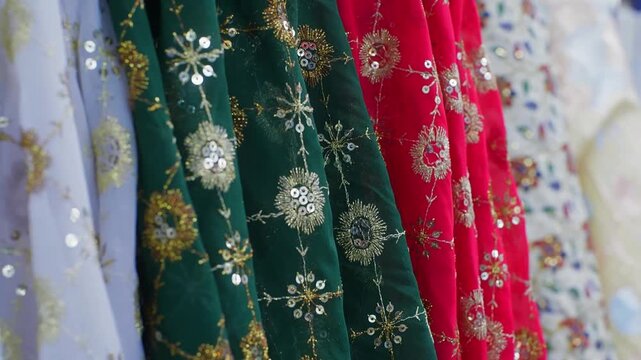 Row of colorful embroidered textiles featuring intricate gold thread designs, sequins, snowflake motifs on white, green, red fabrics in traditional Islamic style.