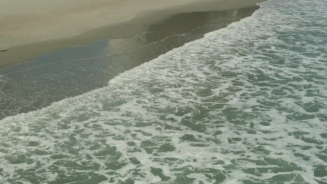 Waves crashing on a sandy beach in a sunny location during the day