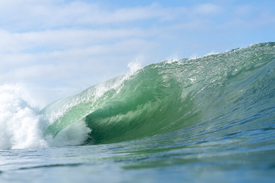 Green Wave Barreling With Blue Sky and Clouds Behind