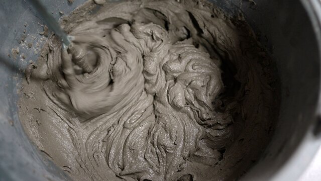 Close up of mixing wet cement mortar in a bucket with an electric paddle mixer for construction work