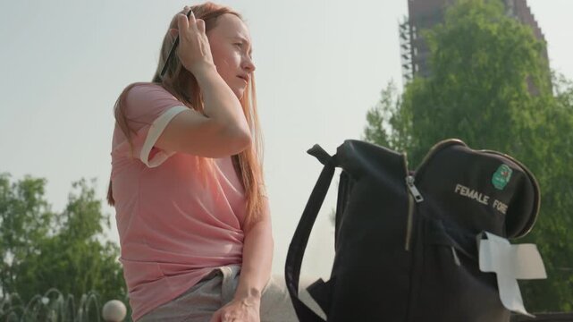 Young woman with long hair writes in notebook while wearing headphones and carrying black backpack labeled FEMALE FORE outdoors. Woman occasionally adjusts her position or touches her face