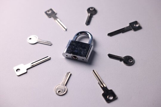Different keys and lock on light grey background, closeup