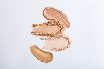 Obraz premium Swatches of different foundations and face powders on white background, flat lay
