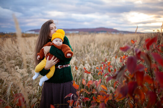 Young mother hugging infant baby girl walking outdoors in fall meadow. Happy loving woman kissing daughter enjoying autumn view