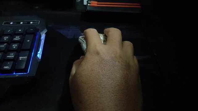 Closeup Hand using a gaming mouse beside an RGB keyboard in a dark computer setup.