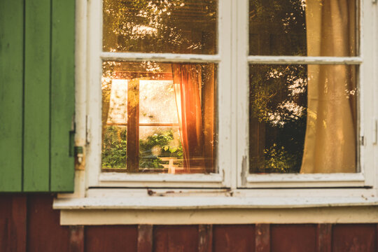 Old cottage window reflecting golden sunlight through curtains.