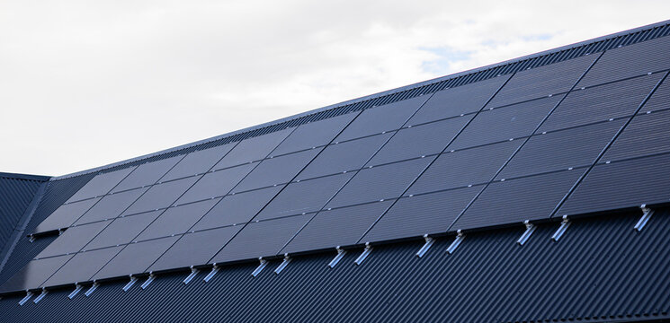 Modern black rooftop solar panels beneath cloudy sky.