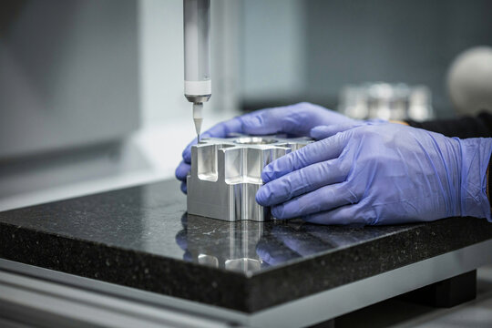Metrology technician measuring a machined aluminium part with a coordinate measuring machine probe