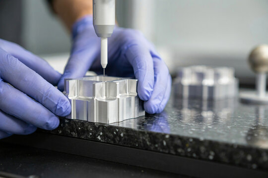 Close up of a CMM touch probe inspecting a milled metal component held in gloved hands