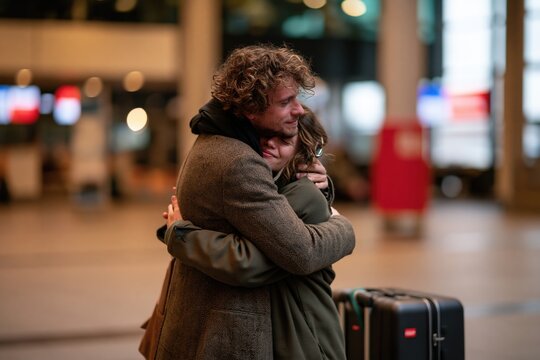 Couple embracing emotionally in airport arrivals hall after long separation