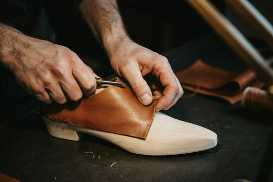 Craftsman shaping leather upper on a shoe last with an awl in a shoemaking workshop