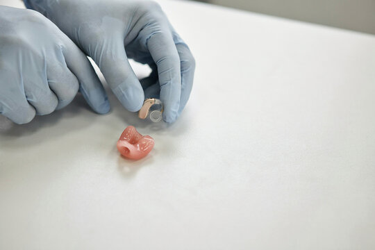 Audiology technician in blue gloves preparing a hearing aid next to a custom ear mould