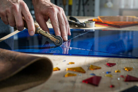 Glass artisan scoring a sheet of deep blue stained glass with a hand cutter