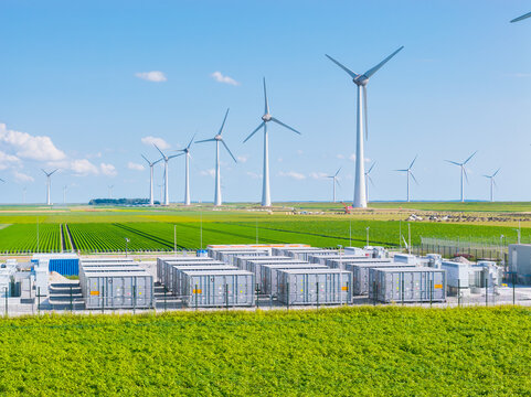 Aerial view of battery energy storage system facility next to wind turbines. Industrial lithium battery system for renewable power plant and grid management.