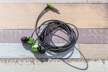 Close up small green and black wired in-ear headphones with magnetic backs attached to each other,...