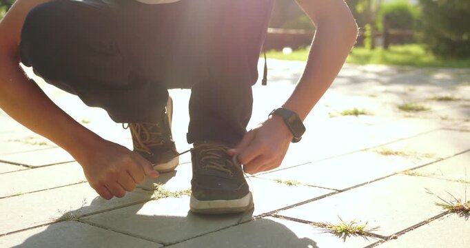 Schoolboy ties shoelaces outdoors in sunlight. Student prepares for school on paved walkway. Independence and childhood focus support positive family back to school campaigns today.