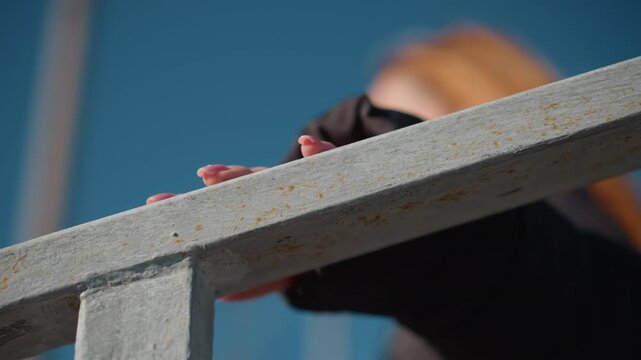 Woman hands with pink nail polish grip weathered metal beam revealing texture and rust details. background is consistently blue throughout sequence suggesting outdoor setting under bright