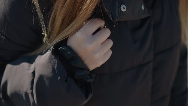 Woman with long hair adjusts her black puffer jacket focusing on hand and fabric details. close up emphasizes texture of synthetic material under natural light showing subtle movement