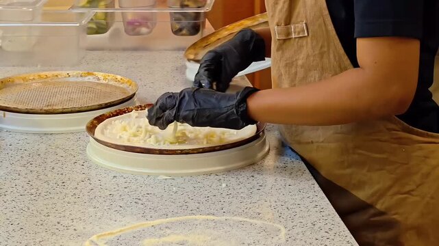 Chef adding parmesan mozzarella cheese topping onto pizza bread dough with white cream sauce, Pizzeria Kitchen Work, Italian Food Preparation, Pastry Making, Bakery Cook