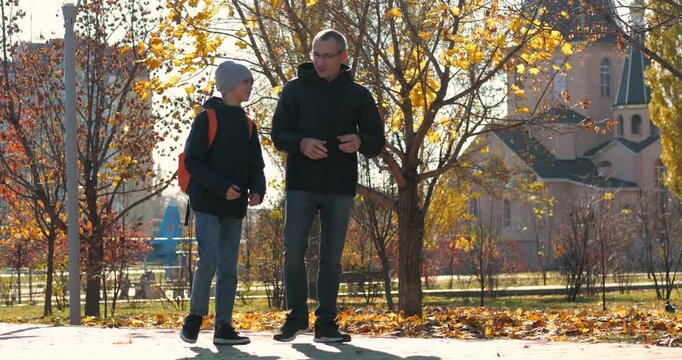 Father and son walking in park during autumn. Dad and boy enjoy conversation and quality time together. Vibrant fall colors create warm atmosphere. Family bonding moment captured.