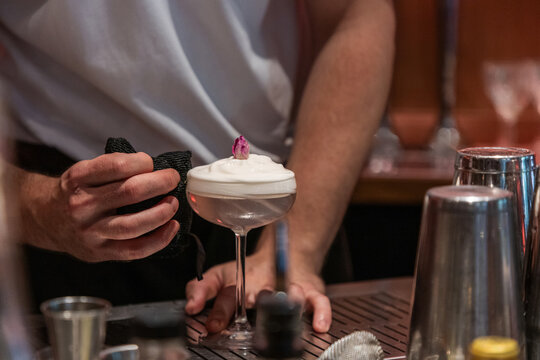Bartender preparing cocktail with foam and decorative flower garnish