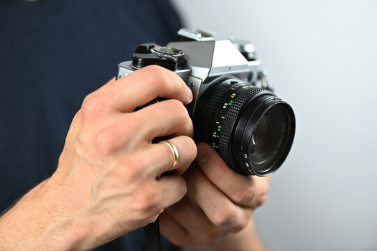 A person is holding an old analog camera in their hand to take a photo. The person's hands are visible as they hold the camera.