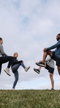 Fitness group members stretching legs together outdoors before group workout