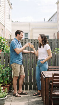 Neighbors toasting drinks together laughing over backyard garden fence
